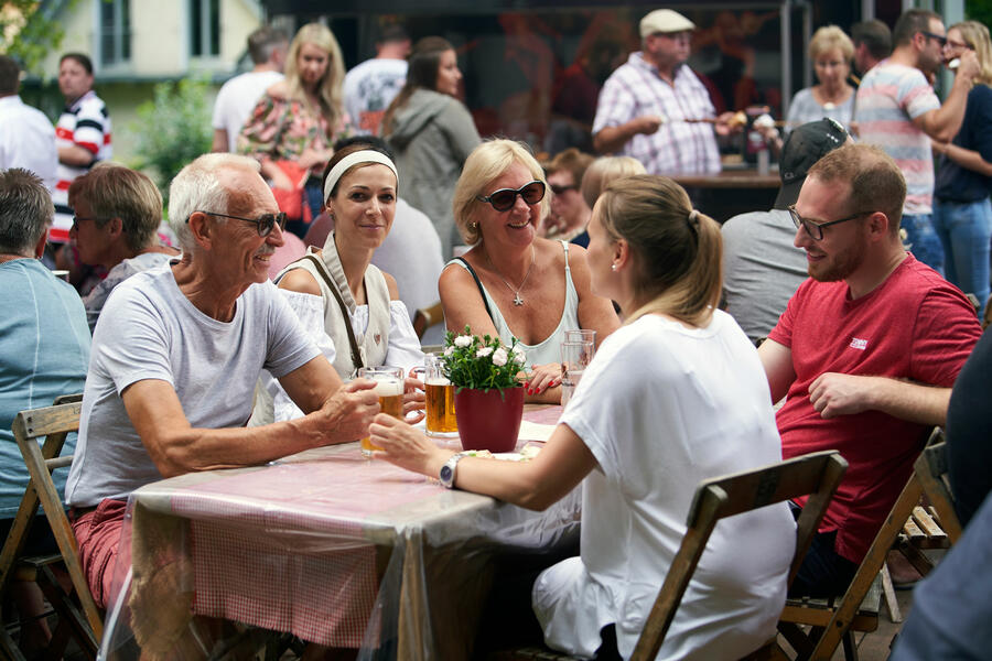 Die Symbolfigur Anneken sitzt gemeinsam mit einer Familie am Tisch bei einem Glas heimischen Bieres in der Gourmetmeile auf dem Annentag