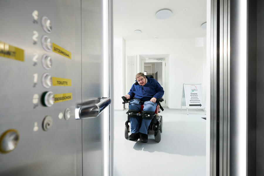 Das Bild zeigt eine Rollstuhlfahrerin vor dem Aufzug in der barrierefreien Verwaltungsnebenstelle, in der sich auch das Bürgerbüro befindet