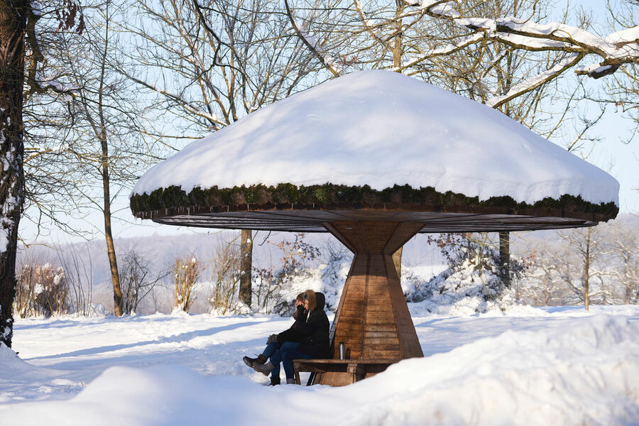 Zwei Frauen sitzen auf einer Bank mit einem pilzartigem Dach im Kurpark Kaiserbrunnen