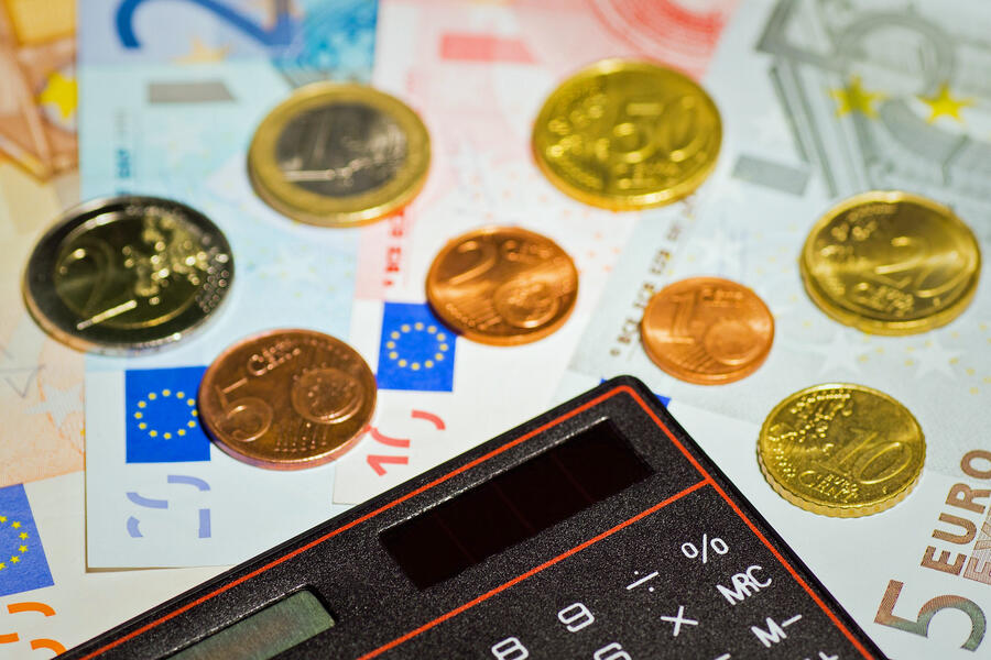 Das Symbolbild zeigt einen Taschenrechner und verschiedene Geldmünzen und -scheine.