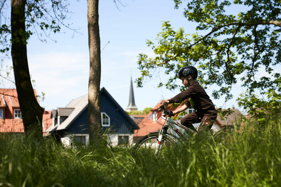Ein Junge fährt auf dem Brakeler Stadtwall Fahrrad, im Hintergrund befinden sich Häuser des historischen Stadtkerns und der Brakeler Kirchturm
