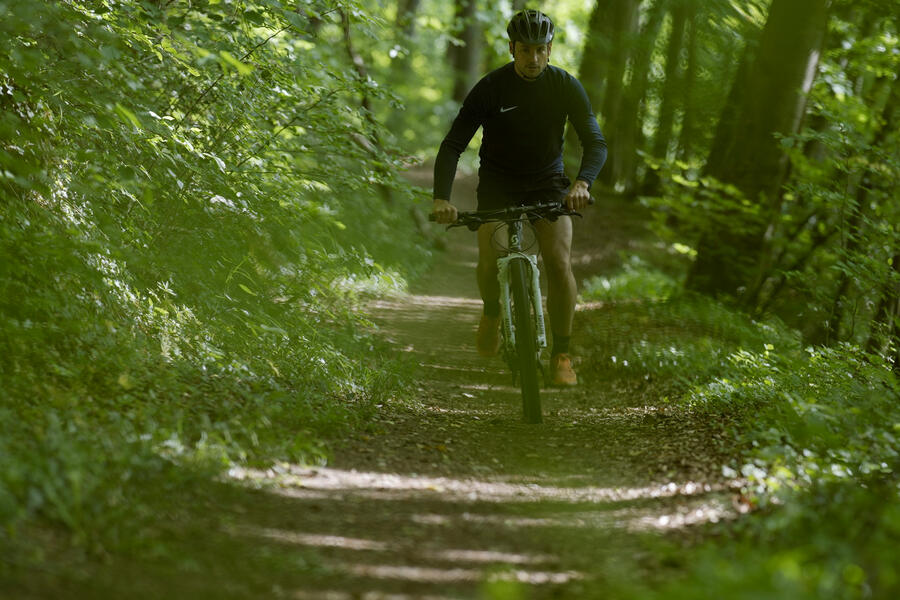 Ein junger Mann fährt mit seinem Mountainbike durch den grünen, sommerlichen Bürgerwald