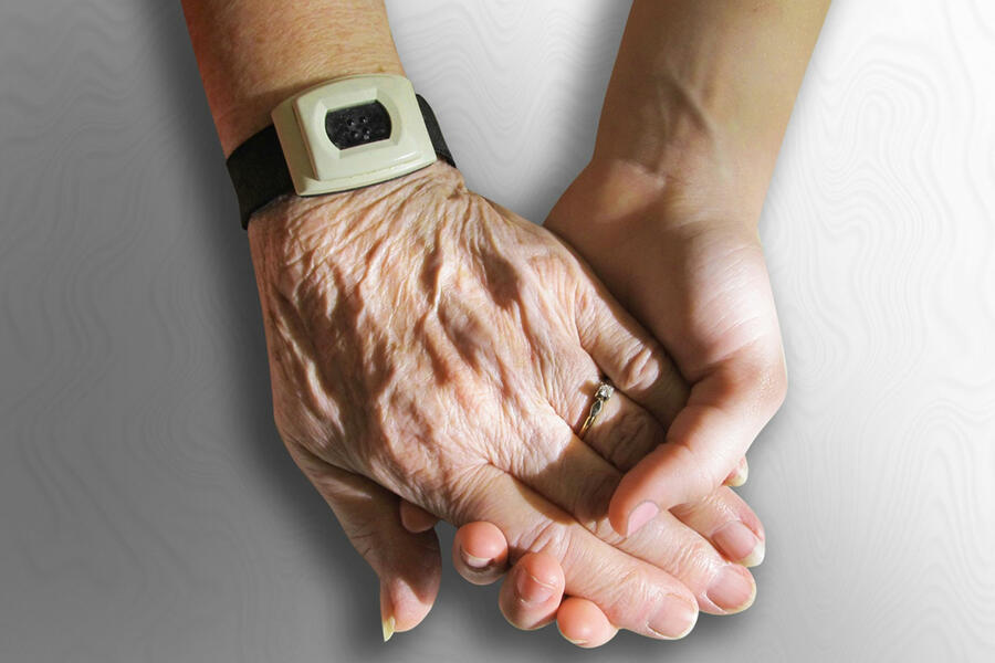 Eine junge Hand hält eine ältere hand als Symbolbild für Pflege im Alter